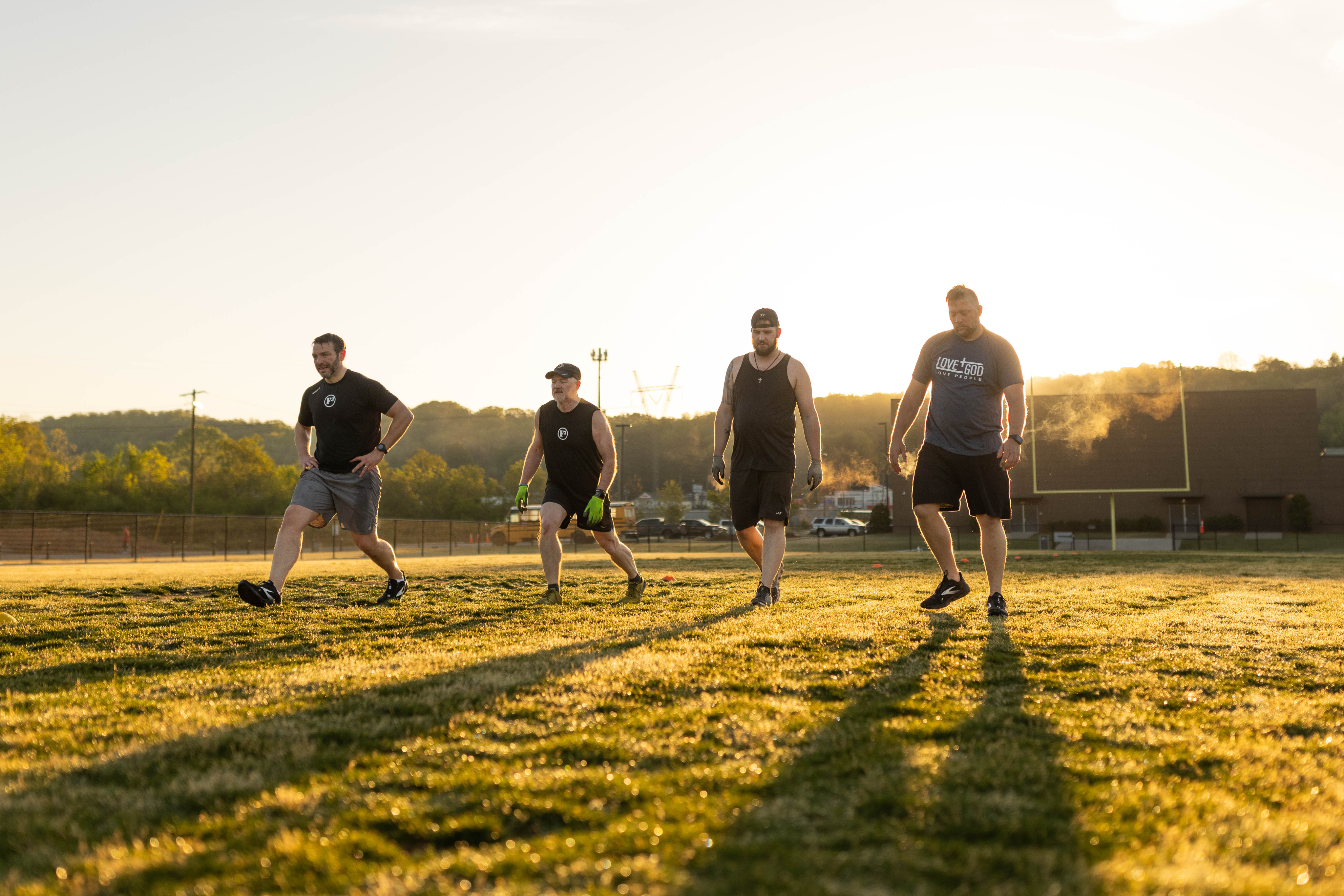 Four men stretching on a field at sunrise